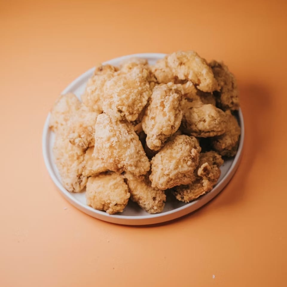A white plate piled high with crispy, golden-brown fried chicken wings on an orange background.