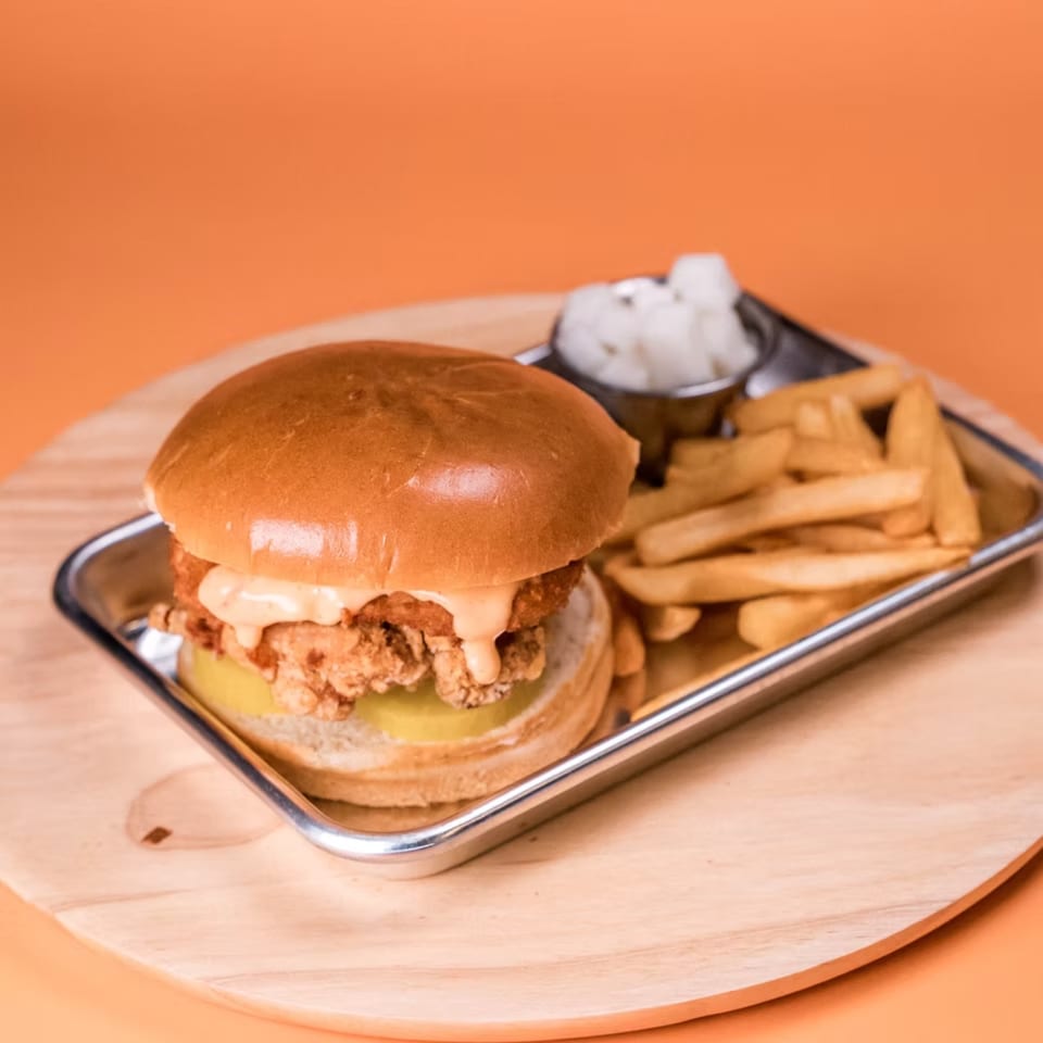 A WingNow fried chicken sandwich with sauce and pickles, served with fries and pickled radishes.