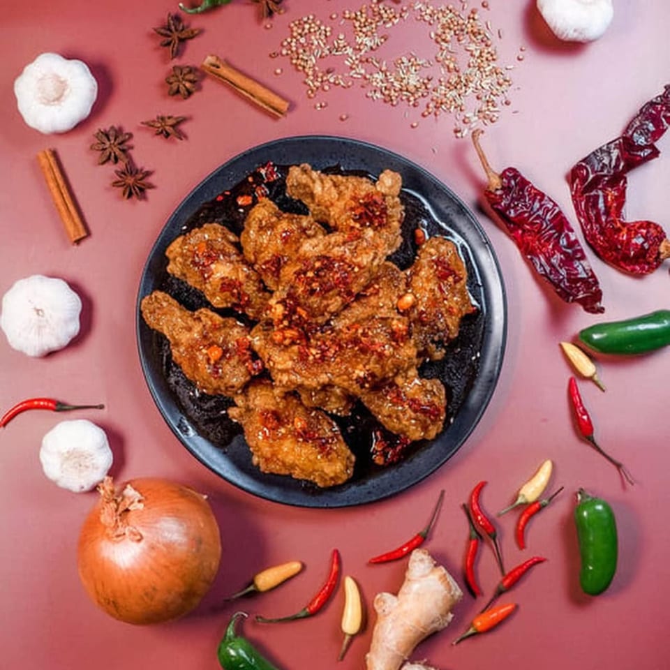 Spicy Asian chicken wings on a black plate, surrounded by garlic, chili peppers, and spices.